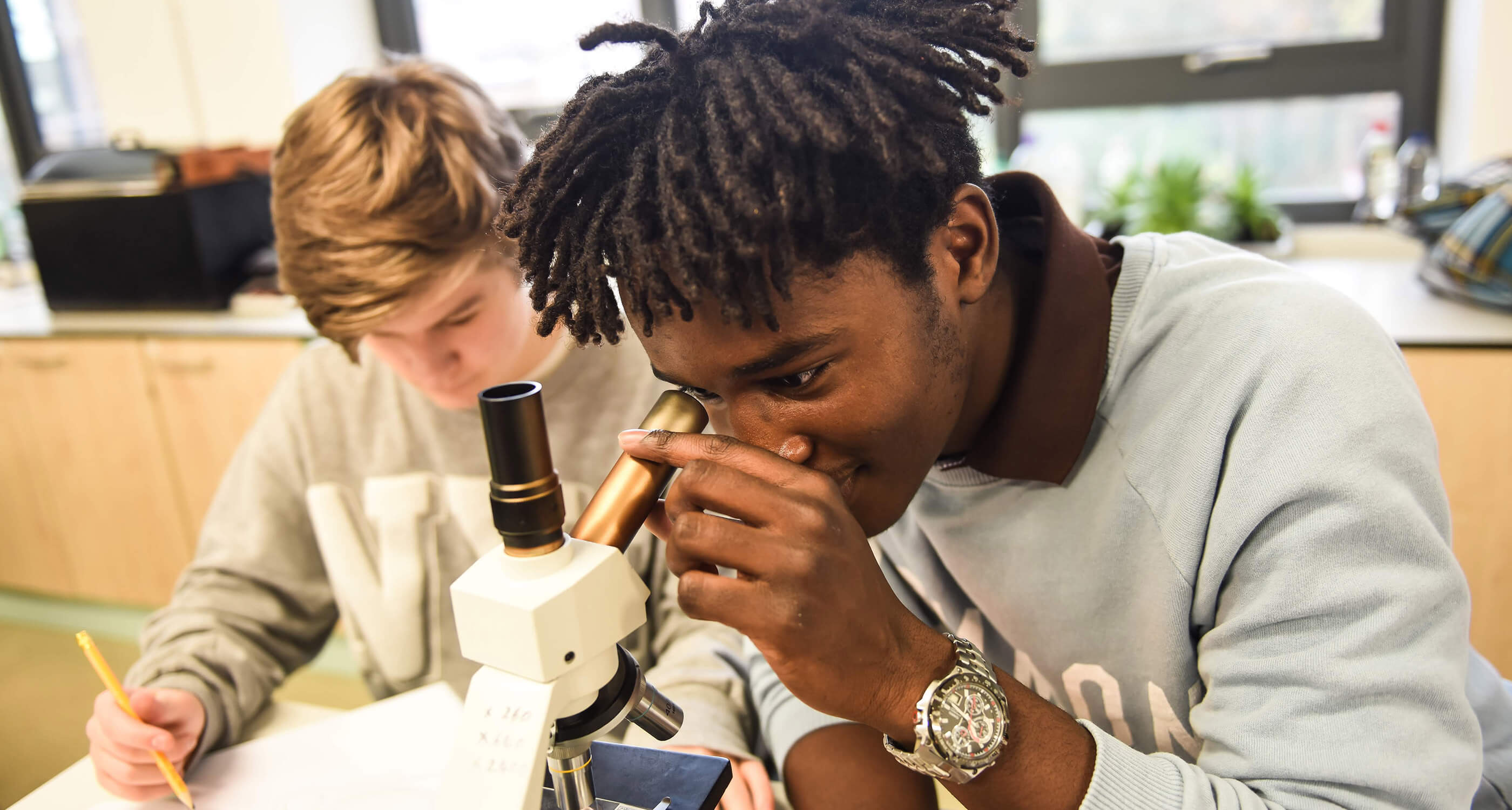 Paston students in science class, one student looking through microscope