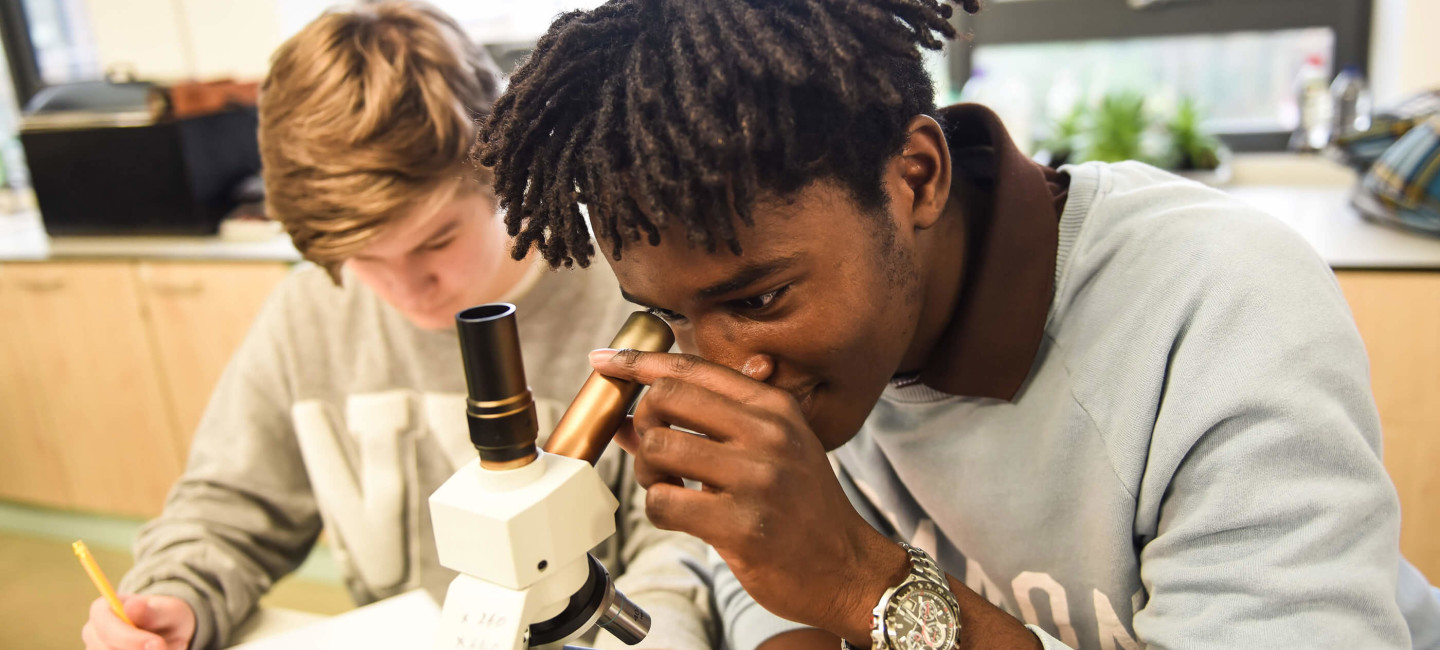 Paston students in science class, one student looking through microscope