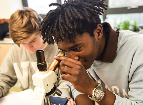 Paston students in science class, one student looking through microscope