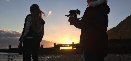 Students filming on beach at sunset