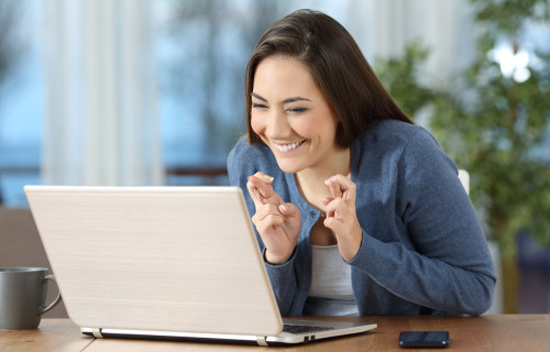 Woman looking at laptop with fingers crossed
