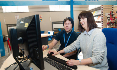 Tutor supporting student at a computer in Paston college library